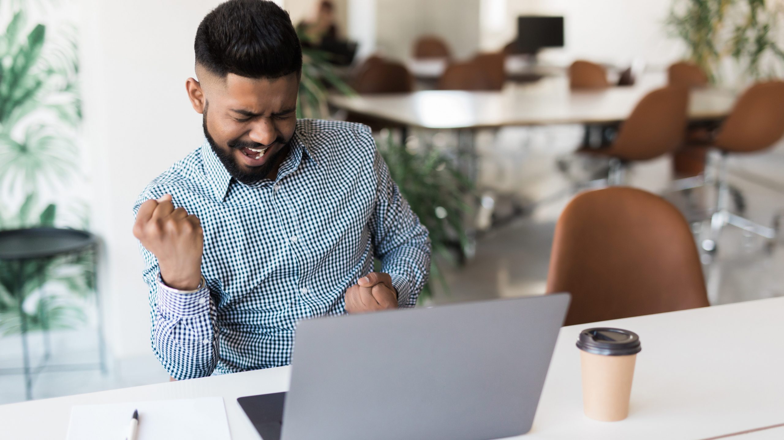 indian businessman and success or victory sign with stretched hands while sitting and looking at computer screen in the office