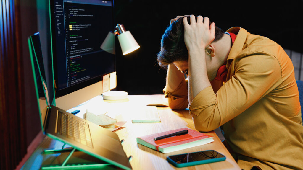 A man in front of a computer with his head down and his hands on his head as if in a state of frustration.